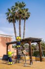 Група робітників у формі та шоломах встановлюють фотоелектричні панелі на даху дерев'яного будівництва біля будинку — стокове фото