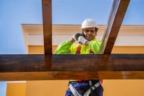 Von unten steht ein männlicher Techniker in Arbeitskleidung auf einem Gerüst und bereitet sich auf die Installation von Solarzellen auf Holzkonstruktion vor — Stockfoto