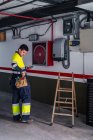 Vista lateral del ingeniero experto hombre en uniforme utilizando el teléfono móvil mientras se examina el equipo eléctrico en el edificio moderno - foto de stock