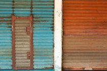 Verwitterte rostige Metall-Rollladentüren in blauer und roter Farbe lackiert mit verschlossener Tür — Stockfoto