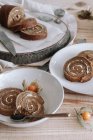 Desde arriba de rebanadas deliciosa torta de rollo dulce casero con crema batida y Physalis flores secas servidas en plato en mesa de madera con ingredientes - foto de stock