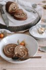 Сверху нарезанный вкусный домашний торт из сладкого ролла со взбитыми сливками и сушеные цветы Физиалиса, подаваемые на тарелке на деревянном столе с ингредиентами — стоковое фото