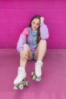 Adolescente na moda com patins sentados perto da parede rosa — Fotografia de Stock
