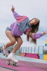 Low angle of modern teen female in bright trendy clothes running on roller skates on colorful playground in city — Stock Photo