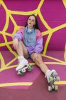 Adolescente na moda com patins sentados perto da parede rosa — Fotografia de Stock
