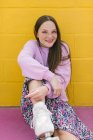 Adolescente alla moda con pattini a rotelle seduto vicino al muro giallo — Foto stock