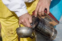 Closeup of crop anonymous male beekeeper making fire on bee smoker while working on apiary — Stock Photo