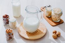 Из вышеуказанного состава стеклянные банки со здоровым веганским молоком помещены на стол с различными орехами и злаками — стоковое фото