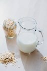 From above of glass jar with healthy vegan oat milk placed on wooden table with pot of oatmeal flakes — Stock Photo