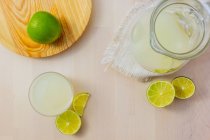 Jug and glass of homemade refreshing lemonade with sliced lime — Stock Photo