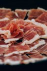 From above view of thin slices of ham with tallow lines served in plate on black background — Stock Photo
