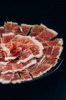From above view of thin slices of ham with tallow lines served in plate on black background — Stock Photo