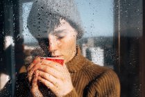 Mujer pensativa bebiendo café cerca de la ventana - foto de stock