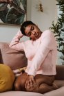 Pensiero annoiato giovane donna afroamericana in abbigliamento casual seduta sul divano mentre trascorreva la giornata a casa — Foto stock