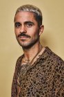 Portrait of cheerful fashionable male model with tattoos wearing trendy leopard shirt standing against beige background and looking at camera — Stock Photo