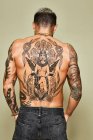 Back view of unrecognizable man with muscular tattooed body in jeans standing against beige background — Stock Photo