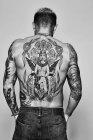 Vista posteriore dell'uomo irriconoscibile con muscoloso corpo tatuato in jeans in piedi su sfondo beige — Foto stock