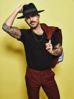 Handsome well dressed male with mustache in trendy hat and vinous suit holding suit coat over the shoulder looking at camera while standing against yellow background — Stock Photo