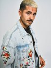 Portrait of young ethnic looking at camera wearing trendy denim jacket with floral pattern while standing against gray background — Stock Photo