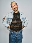 Young ethnic man making grimace face looking at camera wearing trendy denim jacket with floral pattern while standing against gray background — Stock Photo