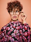 Thoughtful duvidoso bonito encaracolado fêmea em óculos da moda e elegante blusa colorida com ornamento floral olhando para longe contra o fundo rosa — Fotografia de Stock