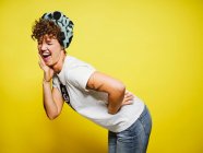 Erwachsene Frauen im trendigen Freizeitoutfit mit Kopftuch mit geschlossenen Augen und lautem Lachen über lustigen Witz, während sie vor gelbem Hintergrund stehen — Stockfoto