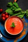 Здоровый домашний томатный суп с хлебом, мятой и оливковым маслом на темном фоне сверху. Концепция веганской еды — стоковое фото
