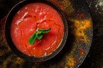 Sopa de tomate casera saludable con pan, menta y aceite de oliva sobre fondo oscuro desde arriba. Concepto de comida vegana - foto de stock