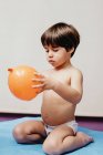 Menino triste sem camisa sentado na cama do hospital e segurando balão laranja enquanto representa o conceito de doença respiratória e tratamento — Fotografia de Stock