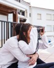 Side view of cheerful romantic couple in casual wear sitting on terrace with binoculars and enjoying view while spending holidays together at seaside — Stock Photo