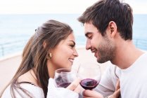 Fröhliches junges Paar in Freizeitkleidung prostet mit einem Glas Rotwein zu und genießt glückliche Momente zusammen — Stockfoto