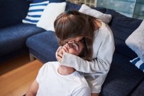 Mujer joven positiva abrazando al hombre feliz mientras está sentado en el sofá en la acogedora sala de estar - foto de stock