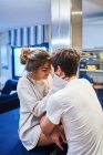 Vue latérale de la jeune femme heureuse assise sur le comptoir de la cuisine et embrassant mari aimant tout en passant la journée ensemble dans un appartement moderne — Photo de stock