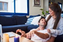 Positive young woman hugging happy man while sitting on sofa in cozy living room — Stock Photo