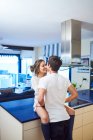 Vista laterale di felice giovane donna seduta sul bancone della cucina e abbracciare marito amorevole mentre trascorre la giornata insieme in appartamento moderno — Foto stock