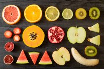 Вид сверху на различные очищенные и срезанные здоровые фрукты и овощи, расположенные на черном светлом столе — стоковое фото