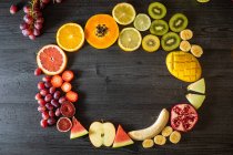Top view of various peeled and cut healthy fruits and vegetables arranged in a circle on a black lumber table — Stock Photo
