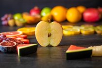 Різні очищені та нарізані здорові фрукти та овочі, розташовані на чорному столі з пиломатеріалів — стокове фото