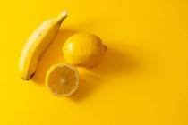 Зверху стиглий банан і свіжий лимон розміщені один біля одного на яскраво-жовтому тлі — стокове фото