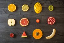 Vista superior de varias frutas y verduras sanas peladas y cortadas dispuestas sobre una mesa de madera negra - foto de stock