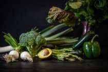 Lot de divers légumes verts placés sur une table en bois sombre sur fond noir — Photo de stock