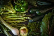 Bunch of various green vegetables placed on dark wooden table on black background — Stock Photo