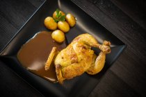 Вид на вкусную жареную курицу и картошку с соусом и петрушкой на стол на черном деревянном столе в ресторане — стоковое фото