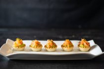 Deliciosas tortinhas com peixe e guacamole dispostos em fileira em placa de cerâmica branca no restaurante — Fotografia de Stock