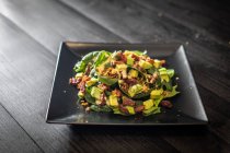 Частина чудового салату з авокадо зі свіжим шпинатом та волоськими горіхами, подається на квадратній чорній тарілці на столі з кафе — стокове фото