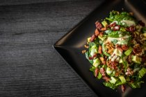 Часть вкусного салата из авокадо со свежим шпинатом и грецкими орехами подается на квадратной черной тарелке на столе кафе — стоковое фото
