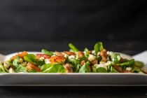 Von oben gesunder Spinatsalat mit Tomaten und Pilzen auf schwarzem Hintergrund — Stockfoto