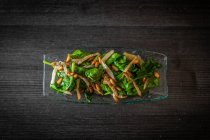 From above glass plate of tasty spinach salad with mushrooms placed on black wooden table in cafe — Stock Photo