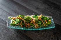 Зверху скляна тарілка смачного салату зі шпинатом з грибами, розміщеними на чорному дерев'яному столі в кафе — стокове фото