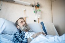 Спокійний літній чоловік з бородою лежить під ковдрою на ліжку в лікарняній палаті і спить — стокове фото